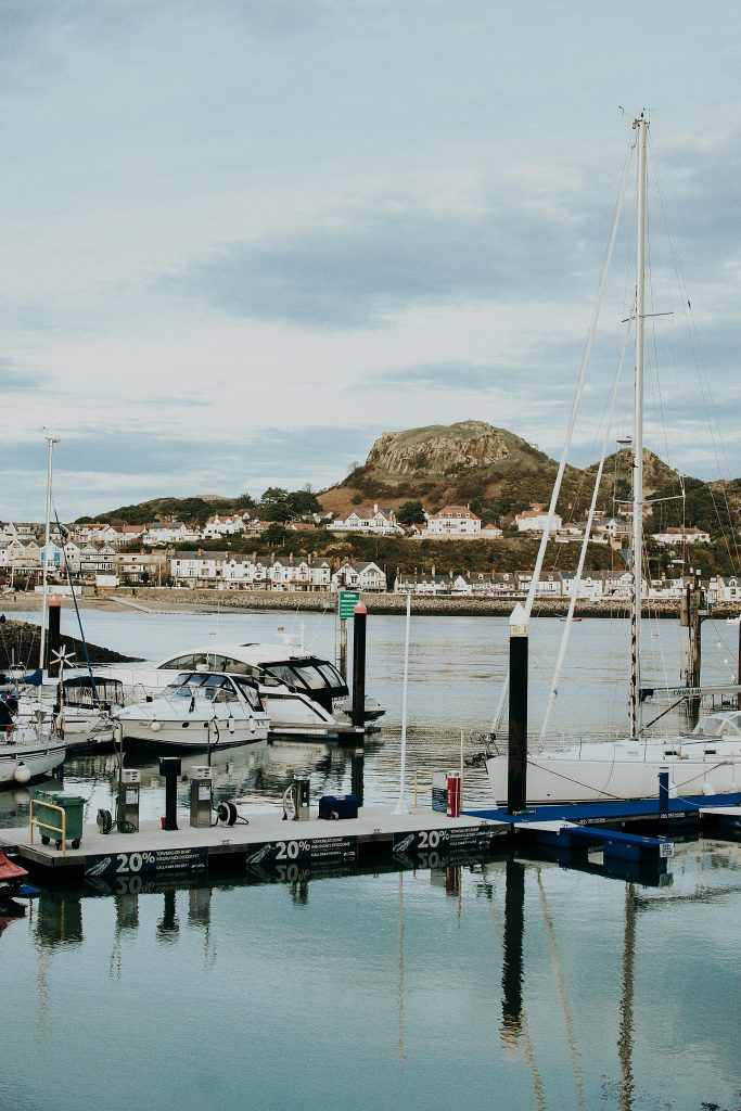 Tranquil UK harbour village with moored boats and whitewashed cottages beneath green hills.