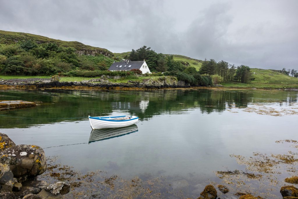 White cottage by a calm lake in the UK countryside, surrounded by hills and reflected in still water - a peaceful hidden family retreat.